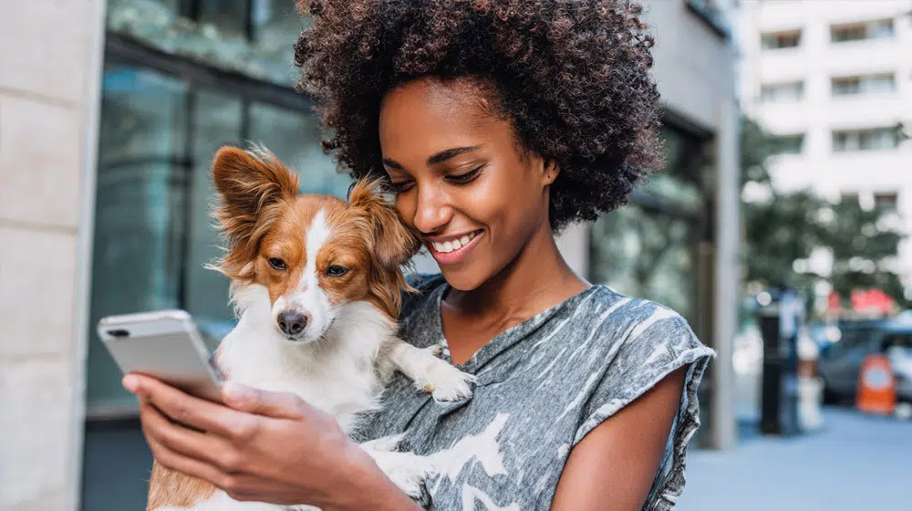 Woman holding her dog while using her phone